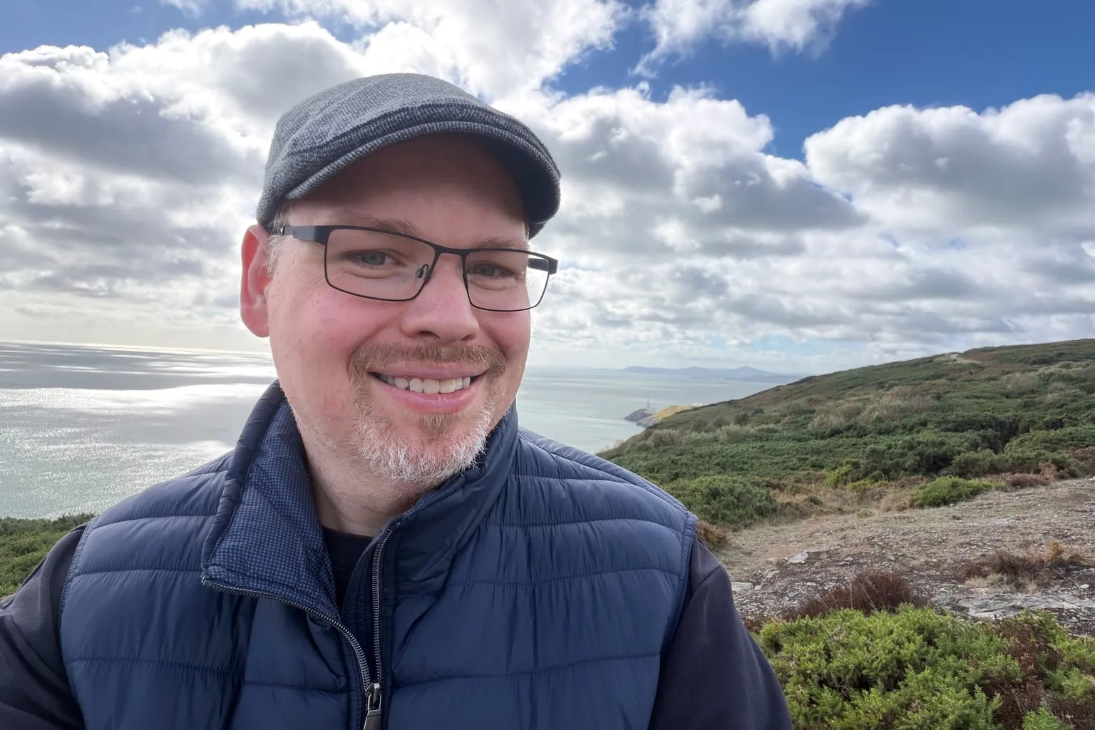 Peter Elst smiling on a coastal hill overlooking the sea.